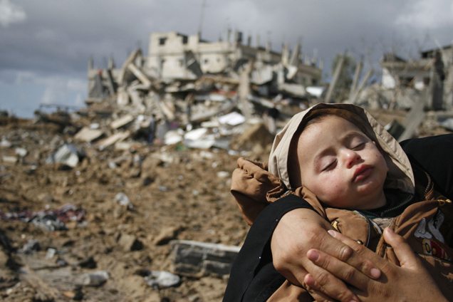 A Palestinian woman carries her baby through the rubble of buildings